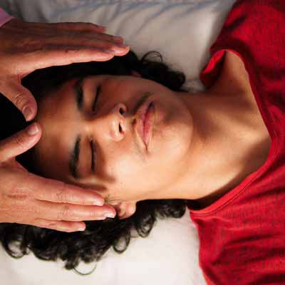 Symbolbild Reiki Mosbach: Männliche Person liegt auf dem Rücken, Hände der Therapeutin werden über dem Kopf gehalten.