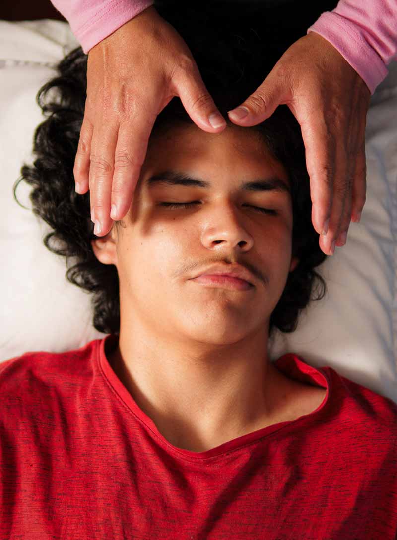 Symbolbild Reiki: Ein Klient liegt auf dem Rücken, die Hände der Heilerin schweben über der Stirn.